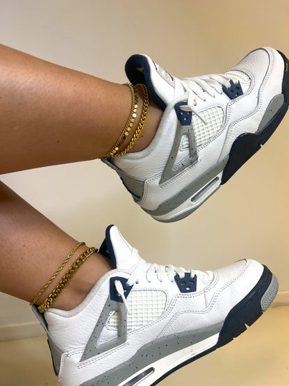 White sneakers with gray and black accents paired with trendy gold anklets, showcasing stylish footwear and accessories against a minimal background.