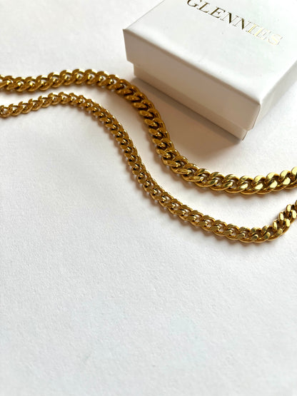 A gold chain elegantly draped with a small white box resting on top, creating a striking contrast.